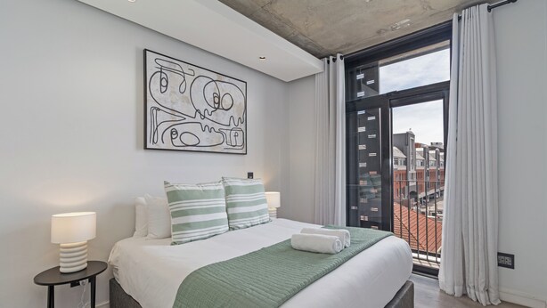 A modern bedroom with a large bed, a view of the city through a balcony, and a unique abstract artwork on the wall. - Stylish Stay at The Signature | Central and Modern (Cape Town)