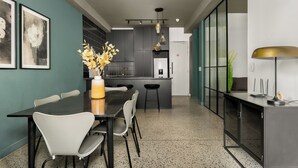 A modern kitchen with a dining area, featuring a black dining table, white chairs, and a vase with flowers. - Trendy CBD Living | Rooftop Pool | Balcony (Cape Town)