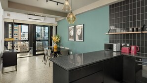 A modern kitchen with a black countertop, a dining area with a table and chairs, and a view through large windows. - Trendy CBD Living | Rooftop Pool | Balcony (Cape Town)