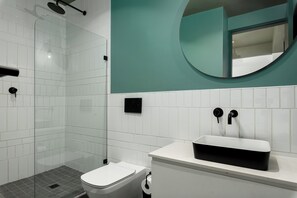 A modern bathroom with a glass shower enclosure, a white toilet, a sink with a black basin, and a teal accent wall. - Elegant CBD Living | Rooftop Pool + Deck (Cape Town)