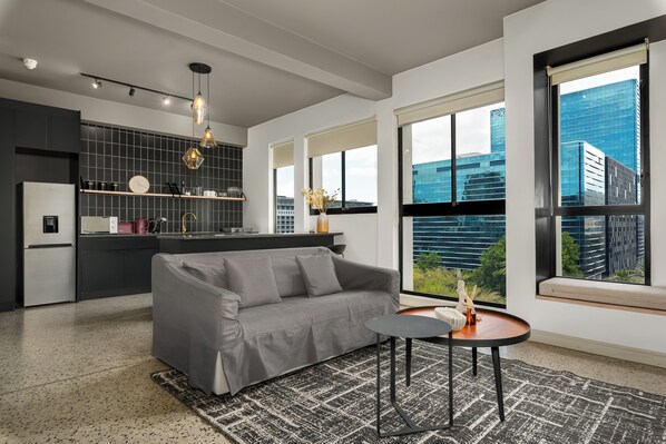 A modern kitchen with a grey sofa, a small table, and large windows offering city views. - Elegant CBD Living | Rooftop Pool + Deck (Cape Town)