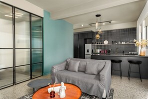 A modern living room with a grey sofa, a round coffee table, and a kitchen area with a black countertop and bar stools. - Elegant CBD Living | Rooftop Pool + Deck (Cape Town)