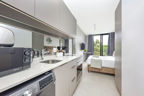 Een moderne hotelkamer met kitchenette, een bed en een groot raam met uitzicht op groen.