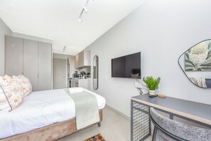 Een moderne slaapkamer met een bed, een bureau, een stoel, een televisie en een plant.