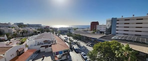 A coastal urban area with a mix of residential and commercial buildings, including a hotel with a red-tiled roof and a large glass facade. - Santa Maria 144 - Two Bed (Costa Adeje)