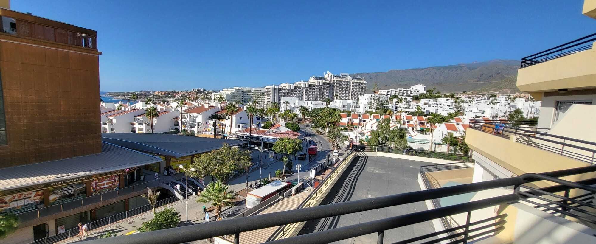 A coastal cityscape with a mix of residential and commercial buildings, a clear sky, and a mountain in the background.