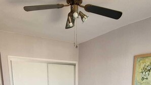 Ett sovrum med två sängar, en takfläkt, en dörr och en väggmonterad lampa.
