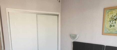A bedroom with two beds, a ceiling fan, a door, and a wall-mounted light fixture.