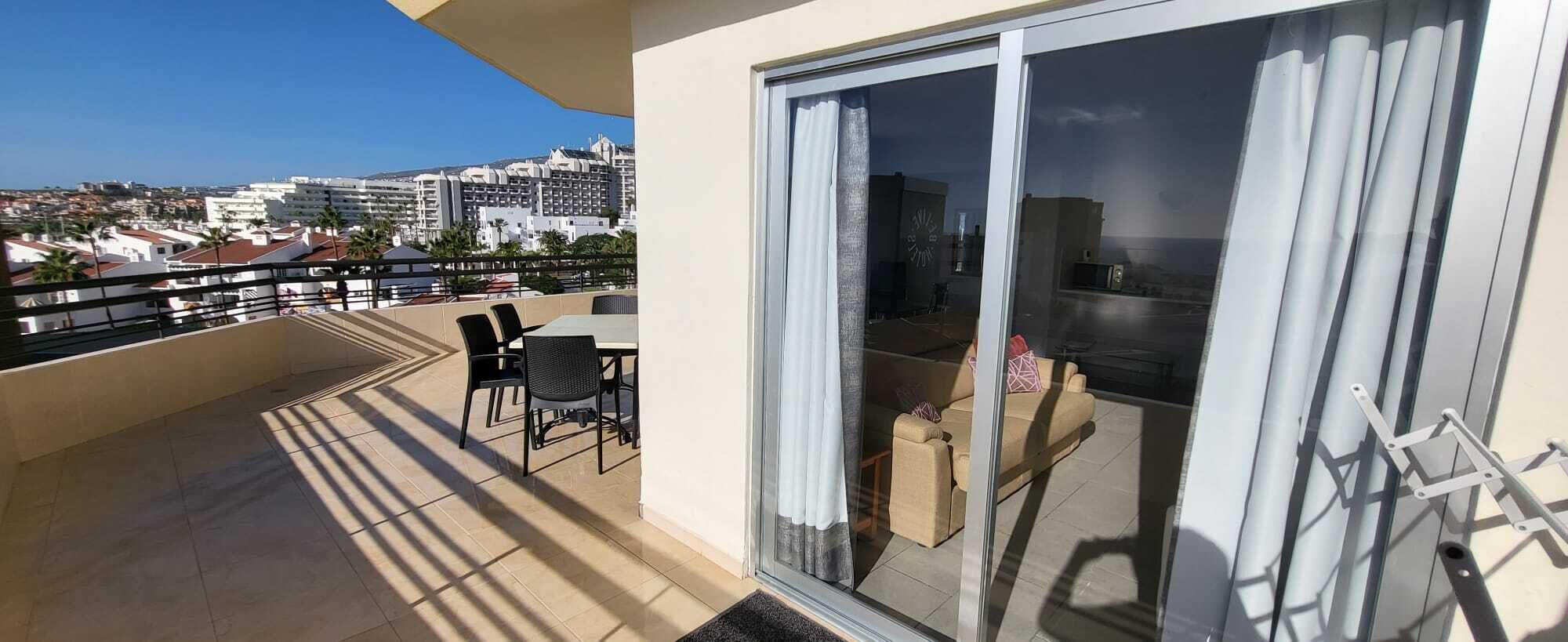 A balcony with a view of a cityscape, a sliding glass door, and a small seating area with a table and chairs.