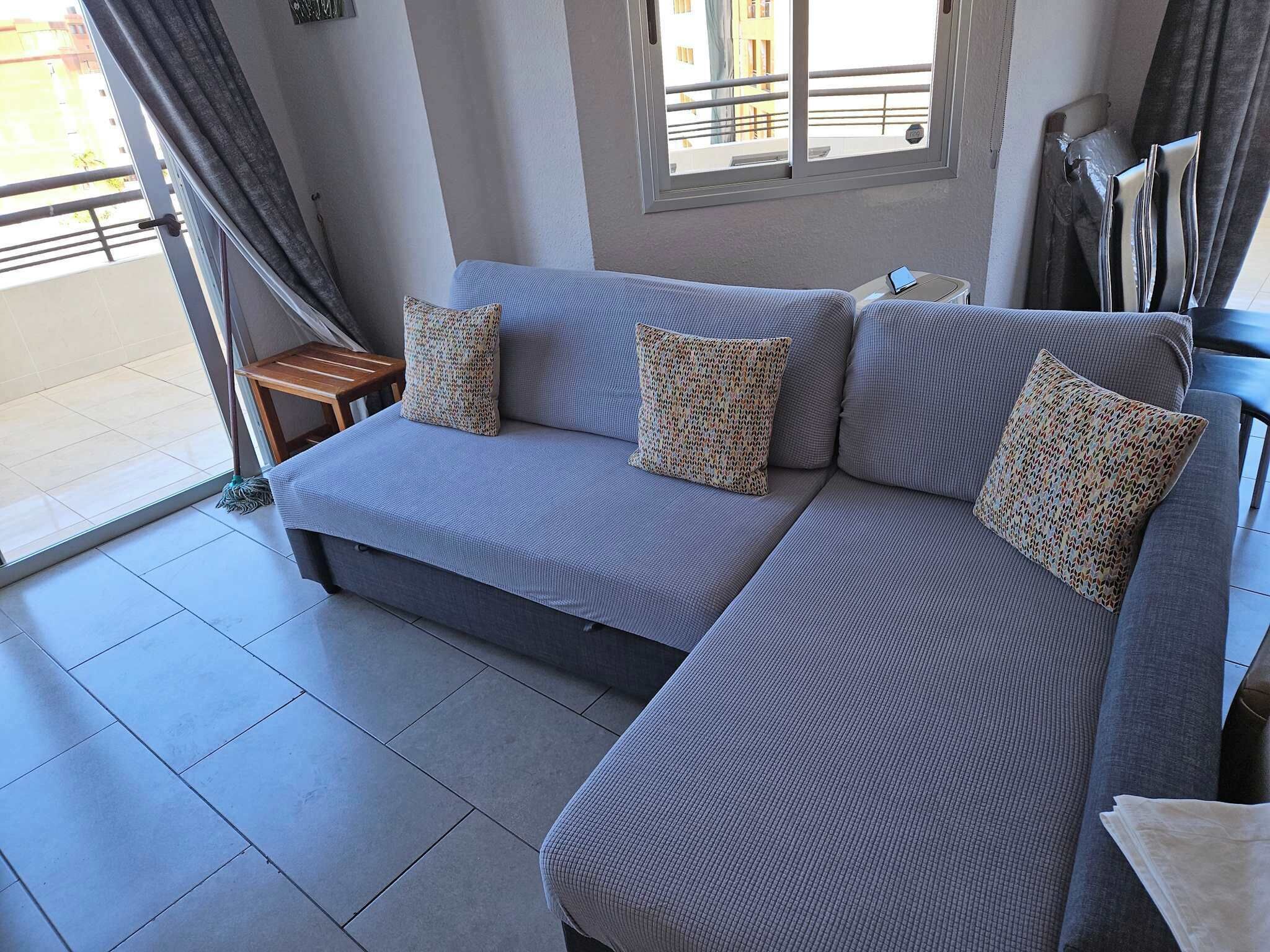Una sala de estar moderna con un sofá seccional gris, cojines estampados, una mesita de madera y vistas al balcón exterior.