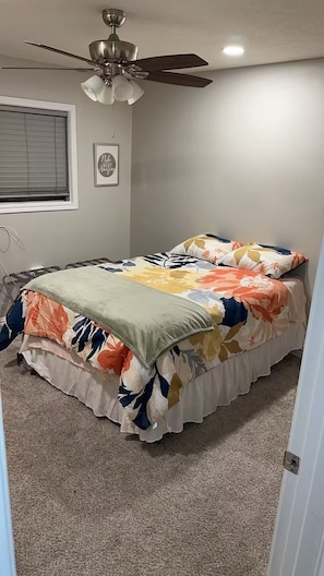 Una camera da letto con un letto, una ventola a soffitto, una finestra con persiane e una citazione motivazionale sulla parete.