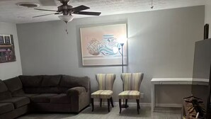 Una sala de estar con un sofá, dos sillones a rayas, un ventilador de techo y un cuadro en la pared.