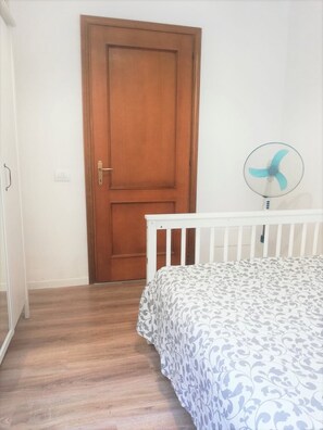 A room with a wooden door, a white crib, and a standing fan. - The Florence Nest B-side (Firenze)