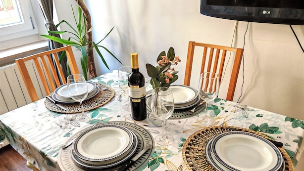 A dining table set with plates, cutlery, and a bottle of wine, surrounded by chairs and a potted plant. - The Florence Nest B-side (Firenze)