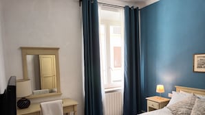 A hotel room with a bed, a desk with a mirror, a chair, a lamp, and a window with curtains. - The Florence Nest B-side (Firenze)