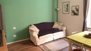 A living room with a green wall, a white sofa with a dark cover, a floor lamp, and two framed pictures. - The Florence Nest B-side (Firenze)