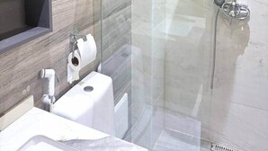 Moderni kylpyhuone, jossa on lasiseinällä varustettu suihku, wc ja peilillä varustettu pesuallas.