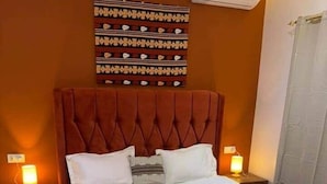 Ein ordentlich bezogenes Bett mit weißen Leinentüchern, einem gepolsterten Kopfteil und zwei Nachttischlampen.