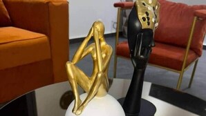Ein modernes Interieur mit einer reflektierenden Oberfläche, einer weißen, kugelförmigen Form und einer goldenen, abstrakten Skulptur.