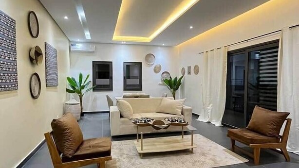 A modern living room with a sofa, two armchairs, a coffee table, and a dining area with a table and chairs. - Almadies Modern 2BR Oasis • Near Beaches & VDN” (Dakar)