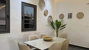 A dining area with a table and chairs, a window, decorative plates on the wall, and a plant. - Almadies Modern 2BR Oasis • Near Beaches & VDN” (Dakar)