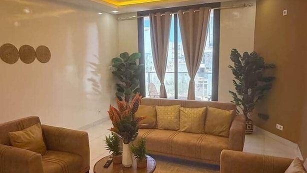 Un salon moderne comprenant un canapé d’angle, deux fauteuils, une table basse et des plantes décoratives.