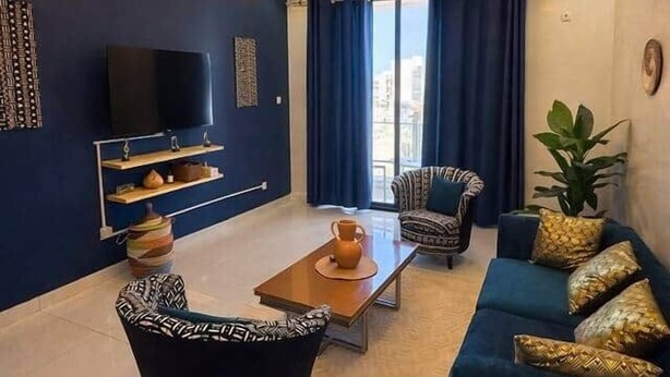 Un salon moderne avec un mur bleu foncé, un téléviseur à écran plat, une table basse, un canapé et un fauteuil à motifs.