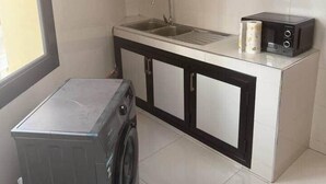 Une cuisine compacte équipée d’un lave-linge, d’un évier et d’un grille-pain.