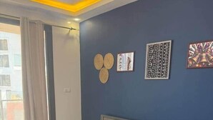 Une chambre avec un grand lit, une porte-fenêtre coulissante et un mur bleu orné d’objets décoratifs.