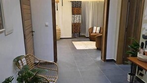 Ein modernes Wohnzimmer mit dunklem Fliesenboden, einer Couch, zwei Korbstühlen und einem Tisch mit Pflanze.