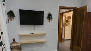 Ein Schlafzimmer mit einem Bett, einem an der Wand befestigten Fernseher, einem Holzschrank und einer Tür zu einem anderen Raum.