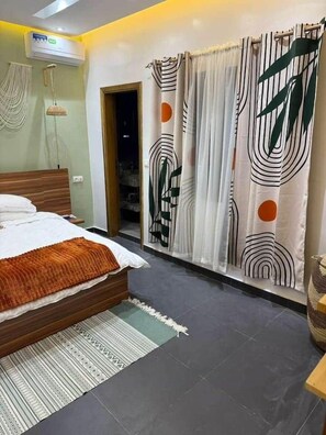 Ein Schlafzimmer mit einem Bett, einem Fenster mit Vorhängen, einer Wand-Klimaanlage und einer Tür zu einem anderen Raum.