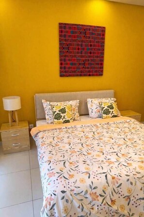 Un dormitorio con cama, dos almohadas, una mesita de noche y una obra de arte en la pared.