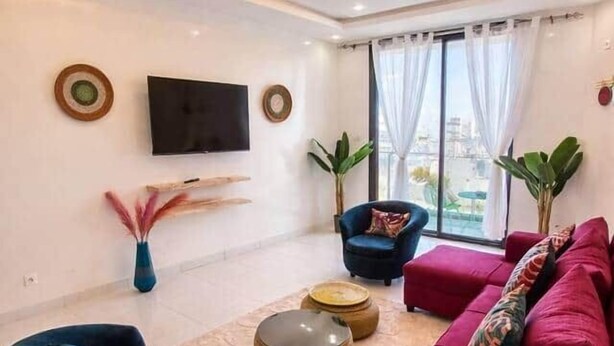 Ein modernes Wohnzimmer mit einem roten Sofa, einem blauen Sessel und einem an der Wand befestigten Fernseher.