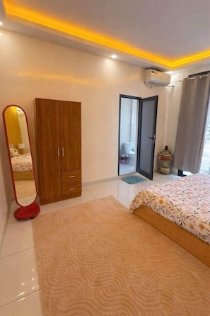 A bedroom with a bed, a wardrobe, a mirror, and an air conditioning unit. - Bright Modern Almadies 2BR | Balcony Dining + Near Beach (Dakar)