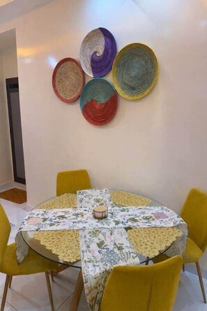 Comedor con una mesa redonda cubierta con mantel floreado, rodeado de sillas amarillas.