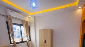 A bedroom with a bed, a wardrobe, and a window with curtains. - Spacious 2BR Almadies • Rooftop • Bright & Breezy (Dakar)