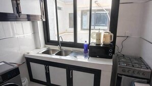 A compact kitchen with a sink, stove, and a window overlooking a parking area. - Spacious 2BR Almadies • Rooftop • Bright & Breezy (Dakar)