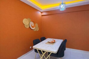 A dining area with a table and chairs, a decorative wall piece, and a hanging light fixture. - Spacious 2BR Almadies • Rooftop • Bright & Breezy (Dakar)