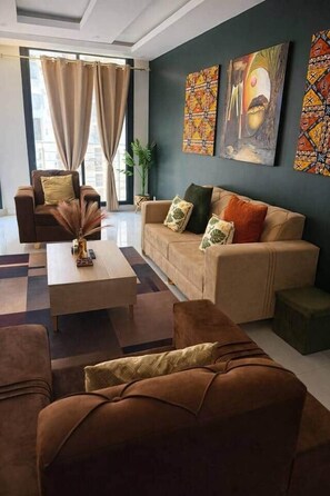 Una sala de estar moderna con sofá, sillón y mesa de centro. Hay cuadros abstractos en la pared y una planta en la esquina.