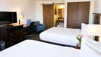 Habitación de hotel con dos camas, un escritorio con silla, televisión, armario y baño visible a través de una puerta abierta.