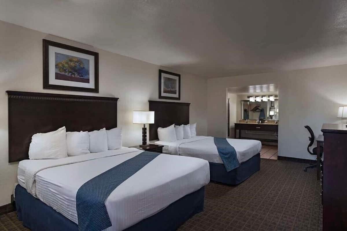 A hotel room with two beds, a desk, a chair, a dresser, and a mirror with lights.
