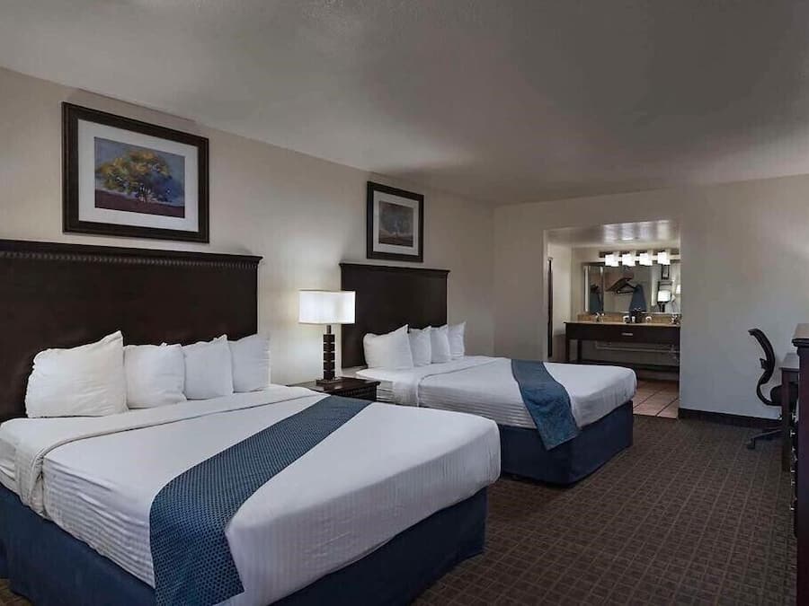 A hotel room with two beds, a desk, a chair, a dresser, and a mirror with lights.