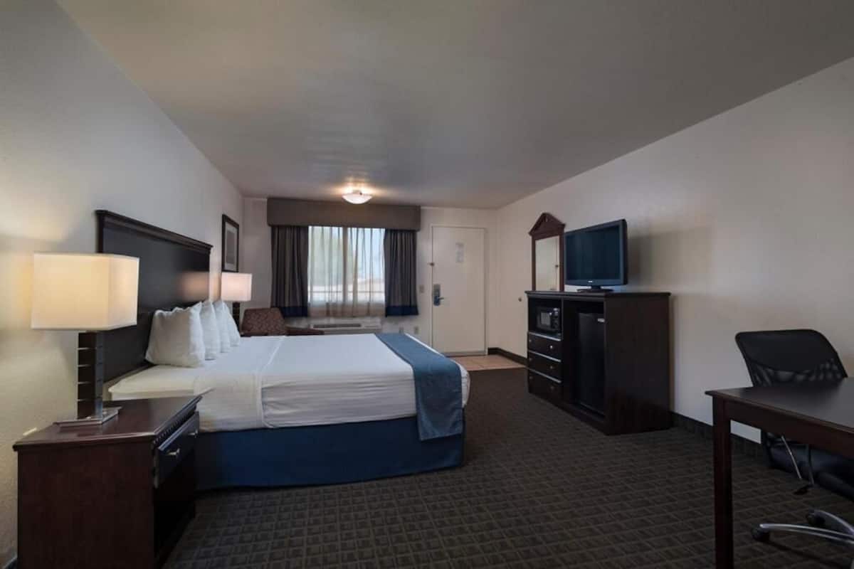 A hotel room with a bed, desk, chair, dresser, TV, and a window with curtains.