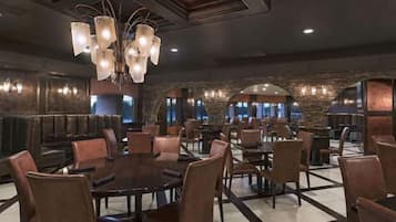 A spacious dining area with multiple tables and chairs, a central chandelier, and stone walls.