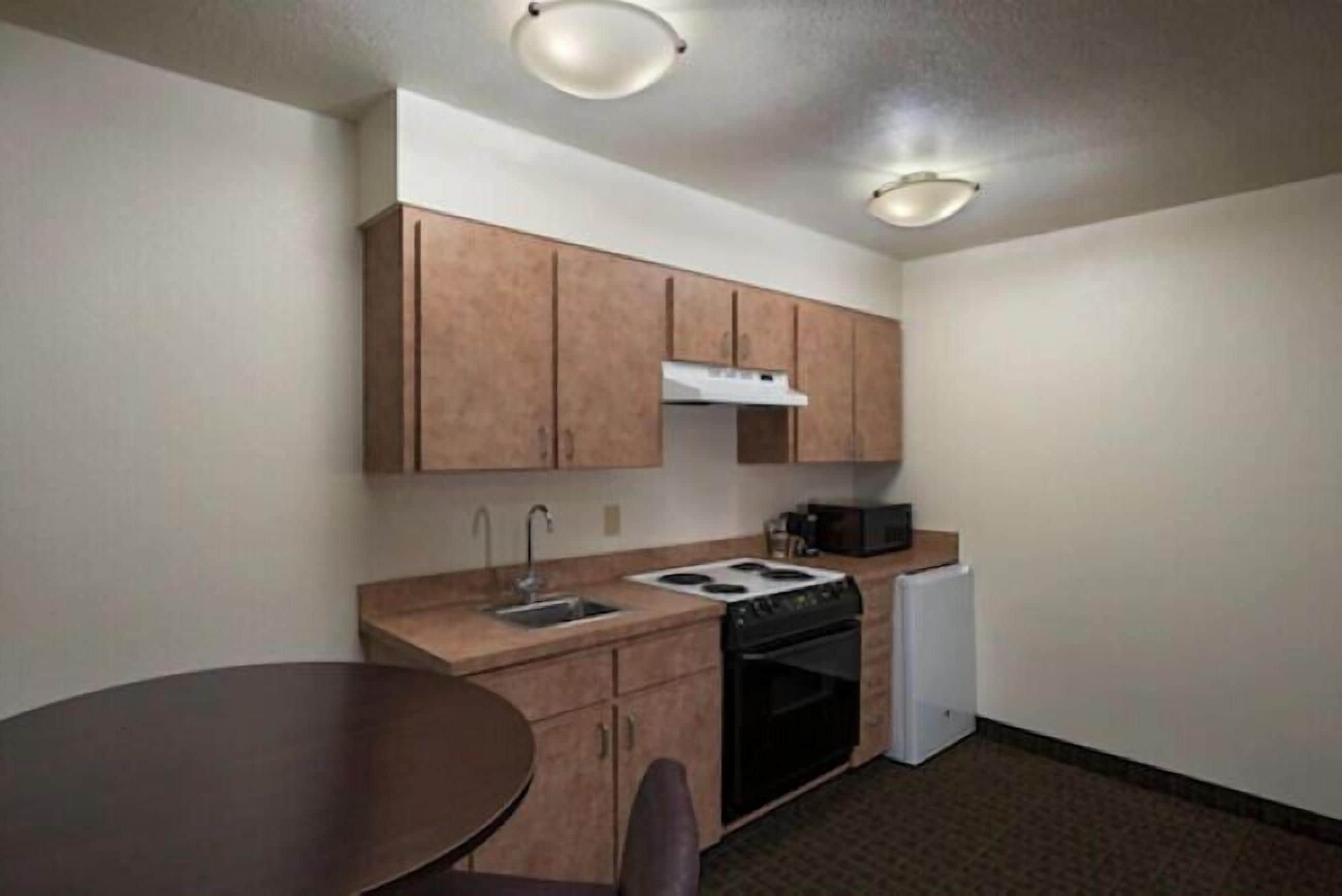 A compact kitchen with wooden cabinets, a stove, a microwave, and a refrigerator.