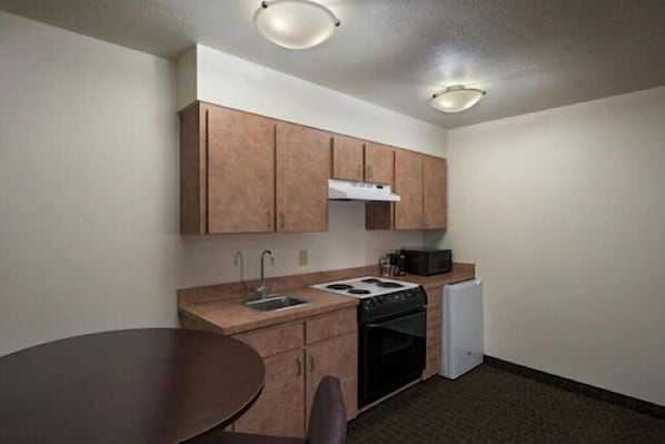 A compact kitchen with wooden cabinets, a stove, a microwave, and a refrigerator. - Stevens Inn (Carlsbad)