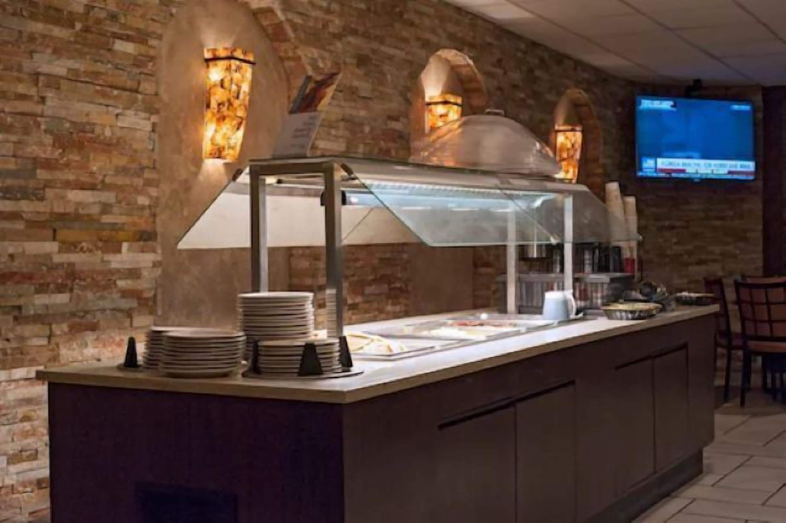 A restaurant with a brick wall, a glass service counter, and a television screen.