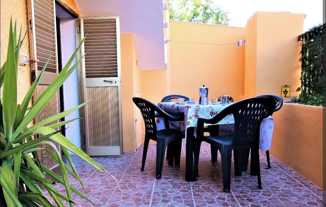 An outdoor patio with a table and chairs, a door with shutters, and a tiled floor.