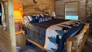 Ein Schlafzimmer in einer Blockhütte mit einem Bett, einem Holz-Kopfteil und einem aufgehängten Hirschkopf.